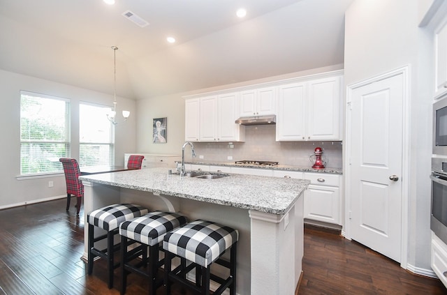 kitchen with white cabinets, a sink, vaulted ceiling, under cabinet range hood, and visible vents