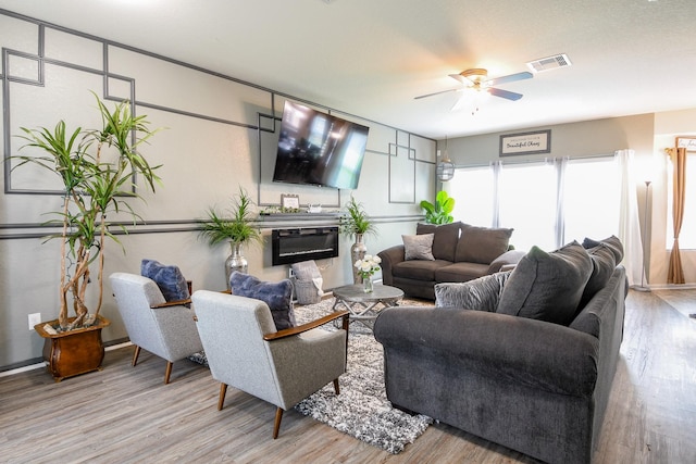 living room with a glass covered fireplace, wood finished floors, a ceiling fan, and visible vents