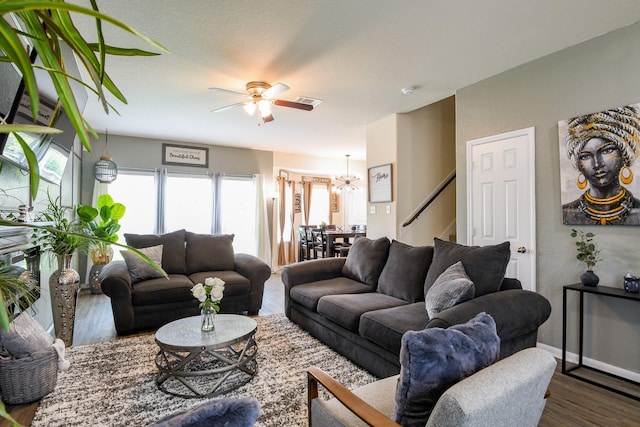 living room featuring stairs, visible vents, baseboards, wood finished floors, and ceiling fan with notable chandelier