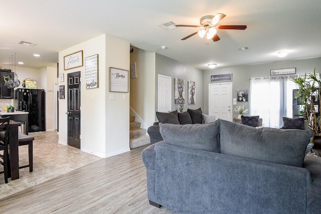 living room with visible vents, a ceiling fan, stairs, and light wood finished floors