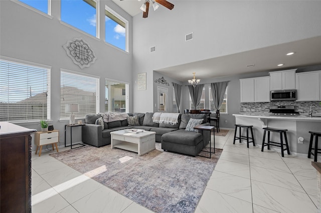 living room with visible vents, ceiling fan with notable chandelier, a high ceiling, and marble finish floor