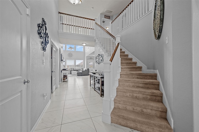 stairway featuring a towering ceiling, visible vents, and baseboards