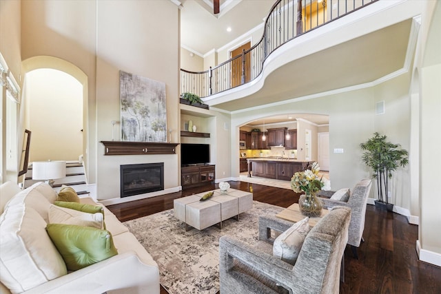 living room with ornamental molding, baseboards, a high ceiling, dark wood-style floors, and arched walkways