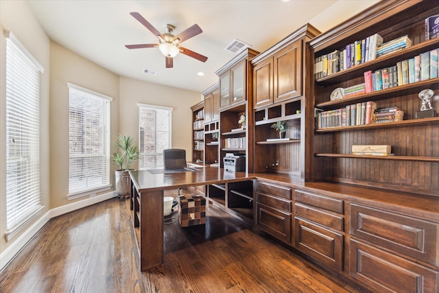 office area featuring visible vents, baseboards, ceiling fan, dark wood-type flooring, and built in desk