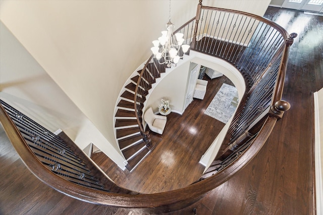 stairs with an inviting chandelier, a high ceiling, and wood finished floors