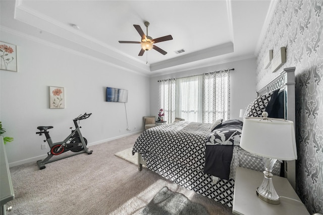 carpeted bedroom with crown molding, visible vents, a tray ceiling, baseboards, and a ceiling fan