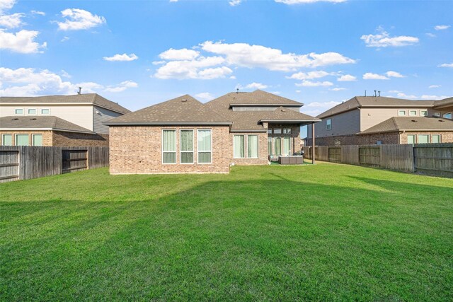 rear view of property with brick siding, roof with shingles, a fenced backyard, and a lawn