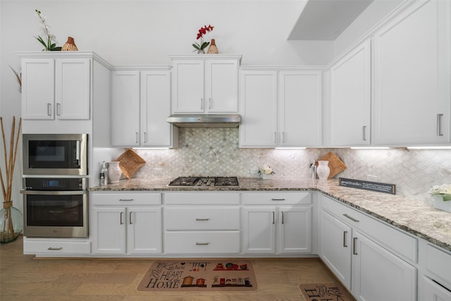 kitchen featuring light stone counters, white cabinets, appliances with stainless steel finishes, under cabinet range hood, and backsplash