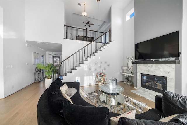living room featuring stairway, ceiling fan, a high end fireplace, wood finished floors, and a high ceiling
