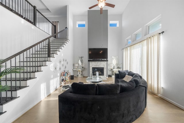 living room featuring ceiling fan, a high end fireplace, wood finished floors, a high ceiling, and stairs