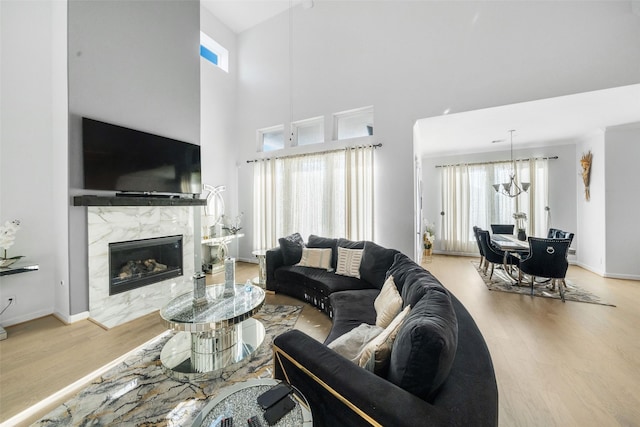 living room with a high end fireplace, baseboards, an inviting chandelier, a towering ceiling, and wood finished floors