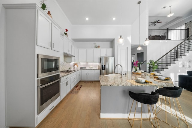kitchen featuring tasteful backsplash, a sink, appliances with stainless steel finishes, light stone countertops, and a ceiling fan