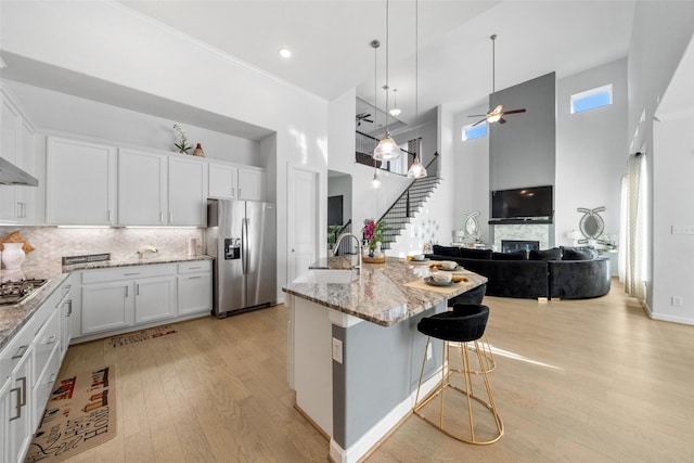 kitchen featuring light stone counters, stainless steel appliances, light wood finished floors, white cabinetry, and a towering ceiling