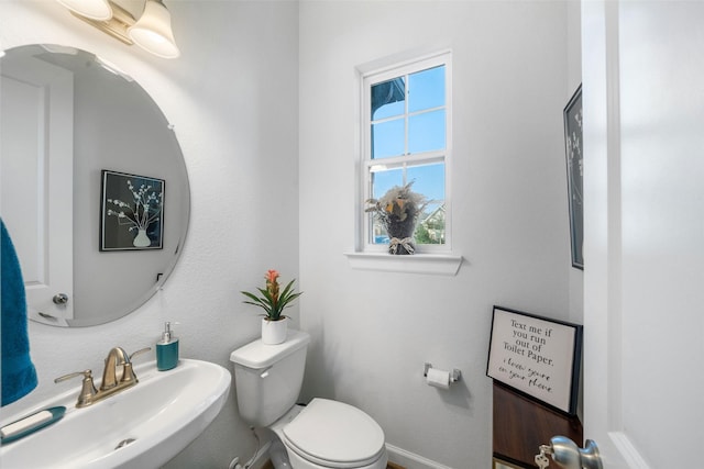 half bathroom featuring toilet, baseboards, and a sink