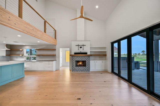 unfurnished living room with a tiled fireplace, high vaulted ceiling, light wood-style flooring, and recessed lighting