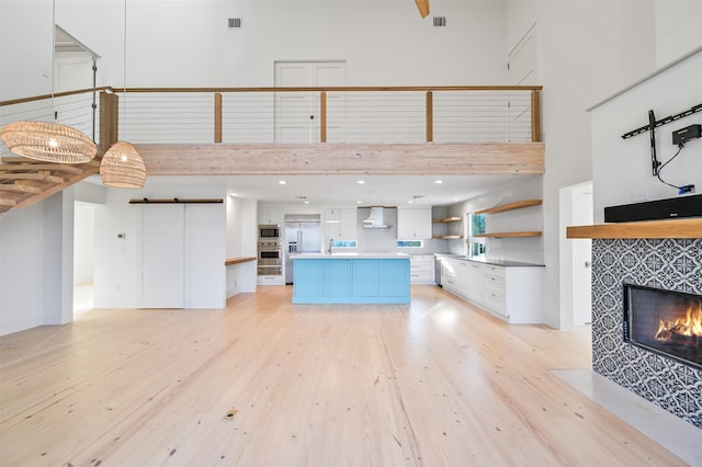 unfurnished living room with a towering ceiling, light wood finished floors, and a tiled fireplace