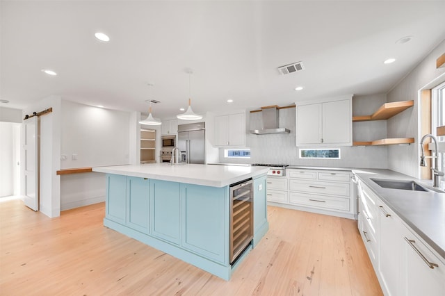 kitchen with a sink, built in appliances, wine cooler, open shelves, and wall chimney exhaust hood