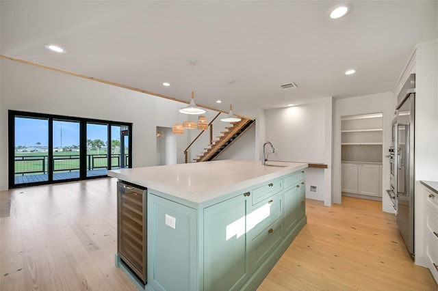 kitchen featuring a sink, beverage cooler, light countertops, light wood-type flooring, and a center island with sink