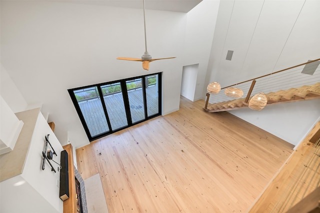 unfurnished living room with wood finished floors, a ceiling fan, and a high ceiling