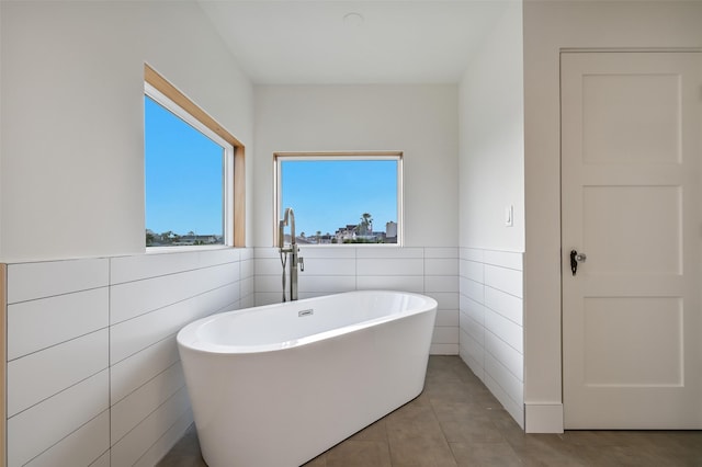 full bath with a soaking tub, a wainscoted wall, tile patterned flooring, and tile walls