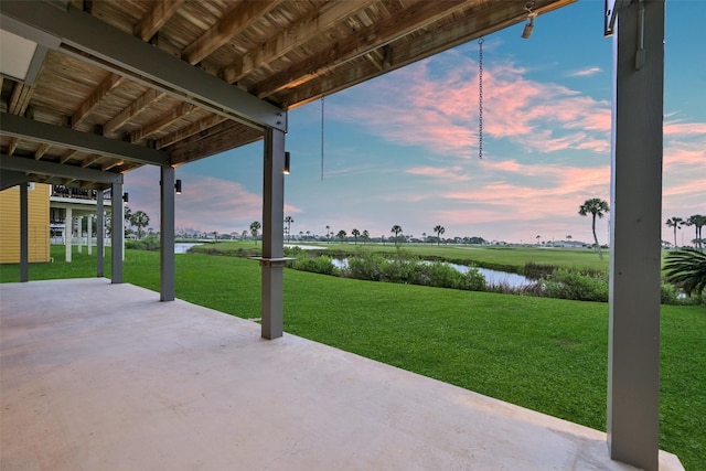 patio terrace at dusk featuring a yard and a water view