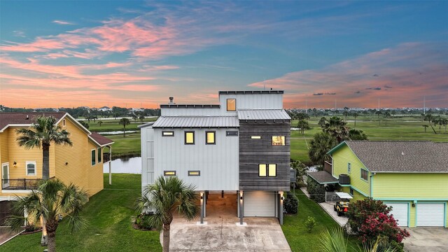 back of house featuring metal roof, a lawn, driveway, a carport, and an attached garage