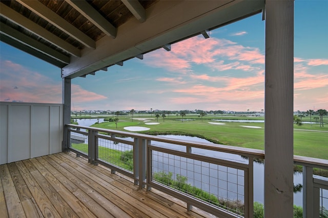 deck at dusk featuring golf course view and a water view