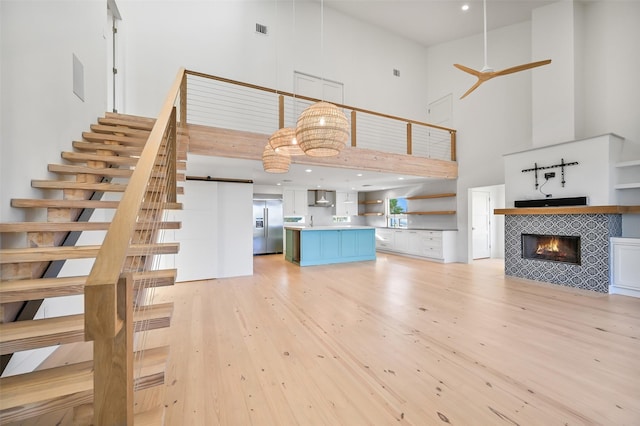unfurnished living room featuring a barn door, light wood-style floors, visible vents, a tile fireplace, and a high ceiling