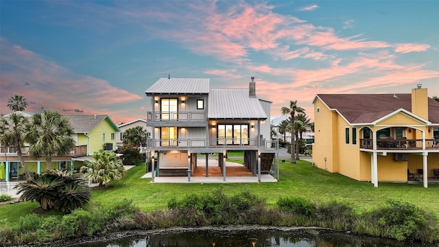 back of property at dusk with a carport, a balcony, a patio area, metal roof, and a lawn