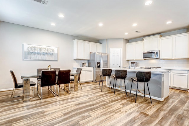 kitchen with tasteful backsplash, a kitchen island with sink, a breakfast bar, stainless steel appliances, and light wood finished floors
