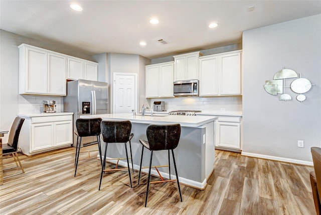 kitchen featuring light wood-style floors, stainless steel appliances, decorative backsplash, and a kitchen bar