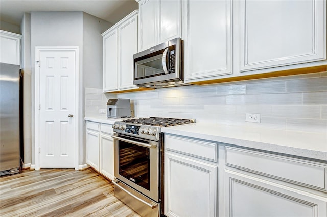 kitchen featuring white cabinetry, stainless steel appliances, light wood-style flooring, and decorative backsplash