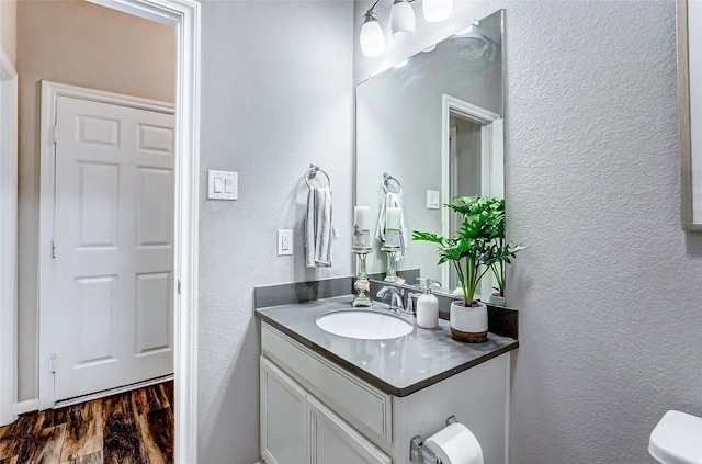 half bathroom with toilet, wood finished floors, a textured wall, and vanity