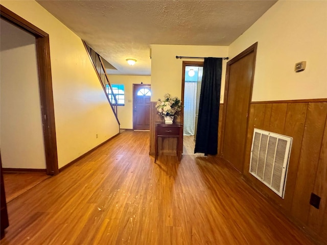entryway featuring wood finished floors, wood walls, a wainscoted wall, visible vents, and a textured ceiling