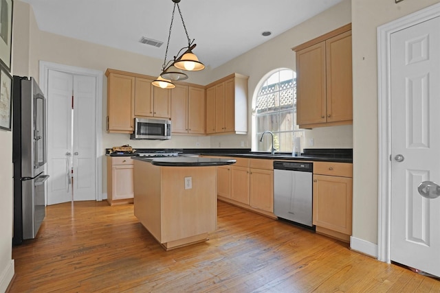 kitchen featuring a kitchen island, appliances with stainless steel finishes, dark countertops, a sink, and light brown cabinets