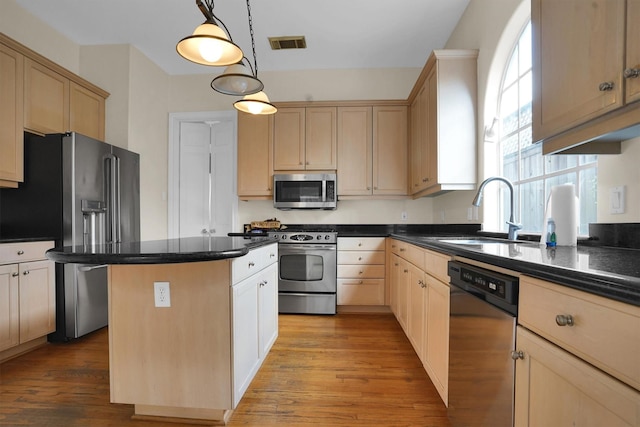 kitchen featuring light brown cabinetry, appliances with stainless steel finishes, a sink, and a center island