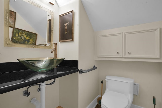 half bathroom featuring toilet, baseboards, vaulted ceiling, and a sink