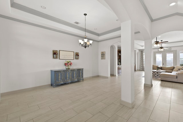interior space with a raised ceiling, crown molding, ceiling fan with notable chandelier, and arched walkways