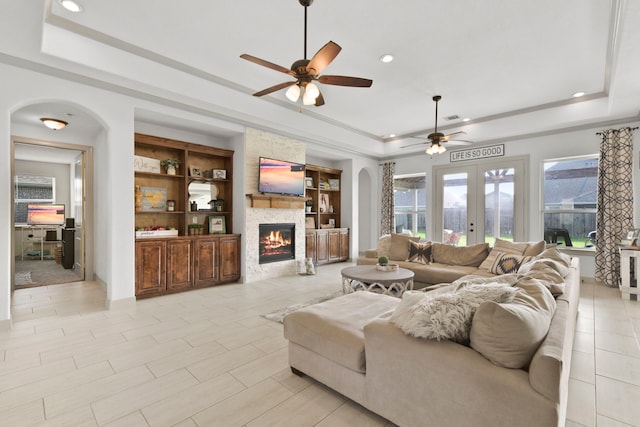 living room with a large fireplace, ceiling fan, recessed lighting, and a tray ceiling