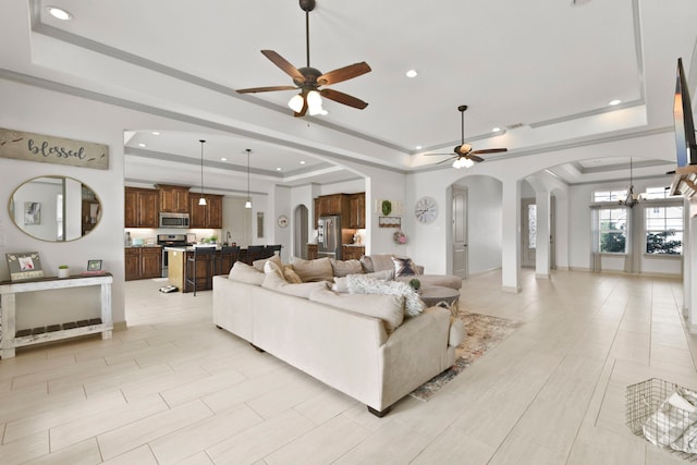 living area with recessed lighting, a raised ceiling, ceiling fan, and arched walkways