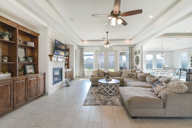 living area featuring ceiling fan with notable chandelier, a tray ceiling, a fireplace, and plenty of natural light