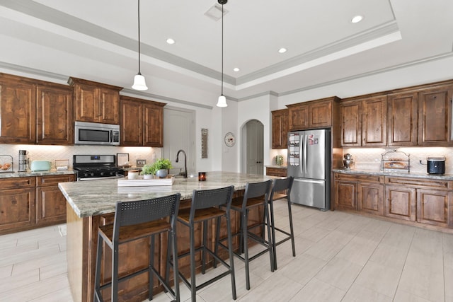 kitchen featuring tasteful backsplash, a breakfast bar, stainless steel appliances, a tray ceiling, and arched walkways