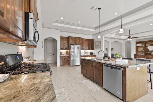 kitchen with arched walkways, appliances with stainless steel finishes, ceiling fan, a sink, and a tray ceiling