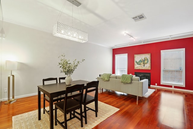 dining space with track lighting, visible vents, wood finished floors, and crown molding