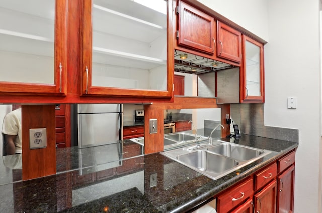 kitchen featuring a sink, glass insert cabinets, backsplash, reddish brown cabinets, and freestanding refrigerator