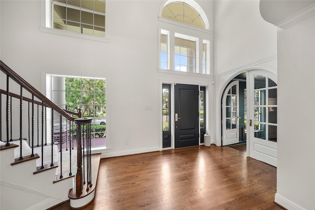foyer entrance with stairway, wood finished floors, and a towering ceiling