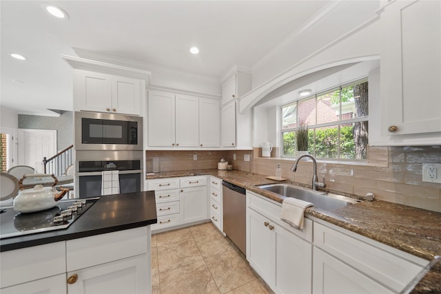 kitchen featuring white cabinets, crown molding, a sink, stainless steel appliances, and tasteful backsplash