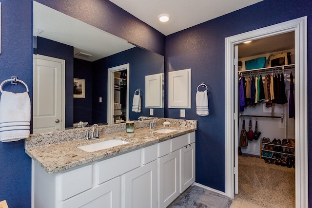 full bath with baseboards, a spacious closet, double vanity, and a sink