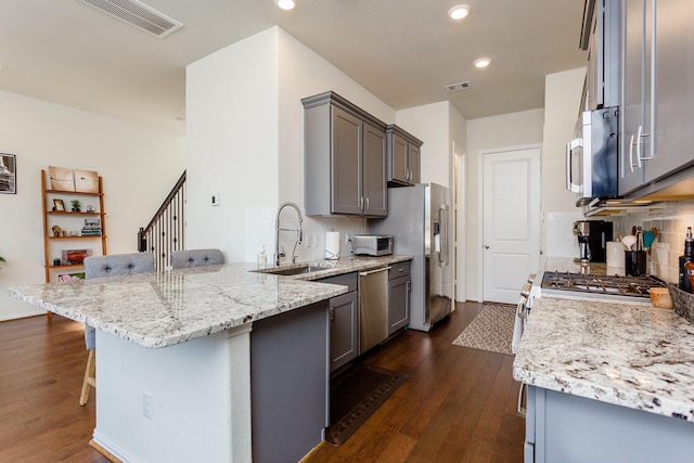 kitchen with a sink, stainless steel appliances, a kitchen breakfast bar, visible vents, and a peninsula