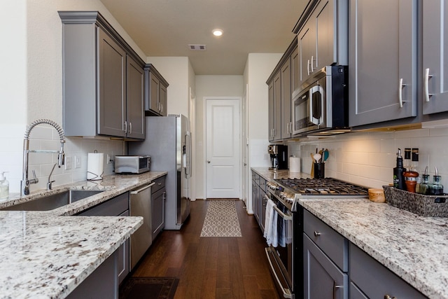 kitchen featuring light stone countertops, a sink, stainless steel appliances, dark wood-type flooring, and backsplash